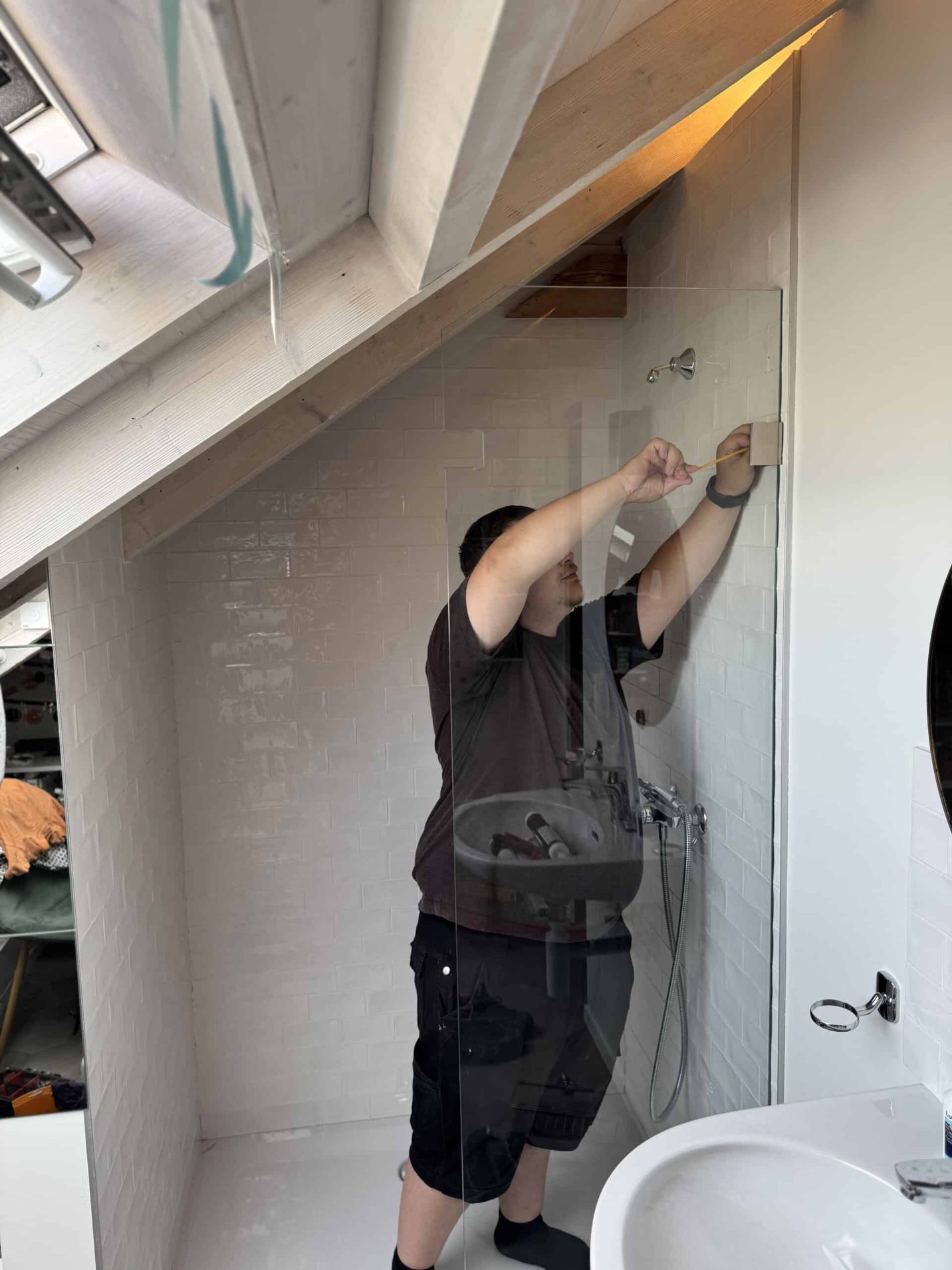 Vitrier installant une paroi de douche en verre sous les combles